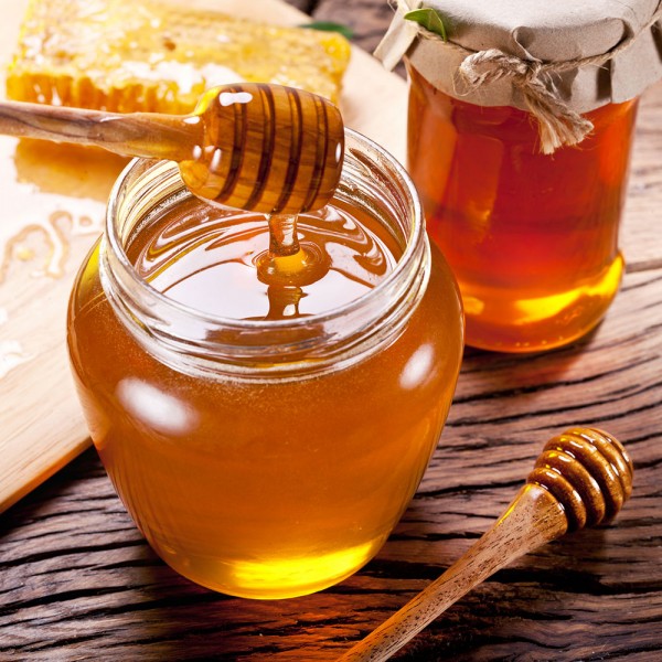 drewniana łyżka do miodu pokryta miodem nad słoikiem miodu